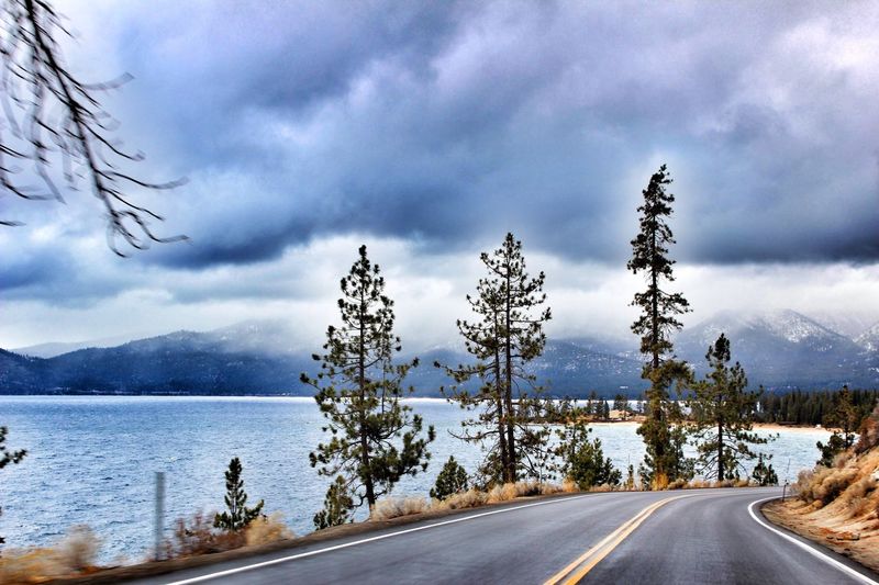 Empty road by lake against cloudy sky