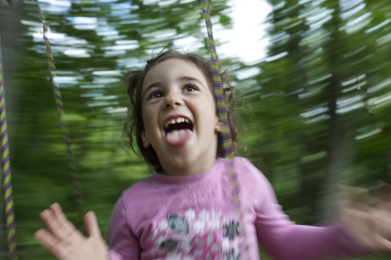 Happy girl sticking out tongue while swinging in forest