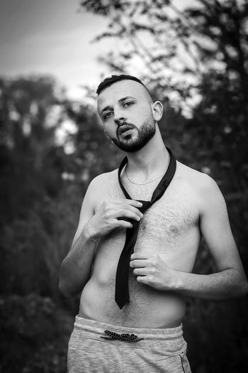 Portrait of young shirtless man standing against trees outdoors