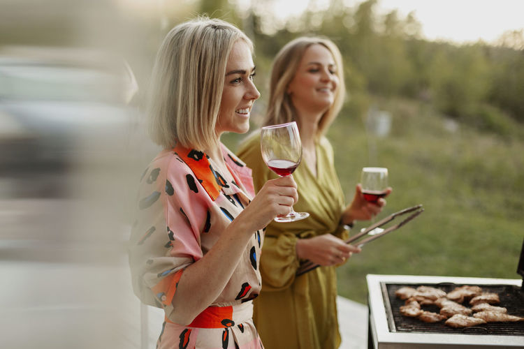 Female friends holding wine glasses and barbecuing meat