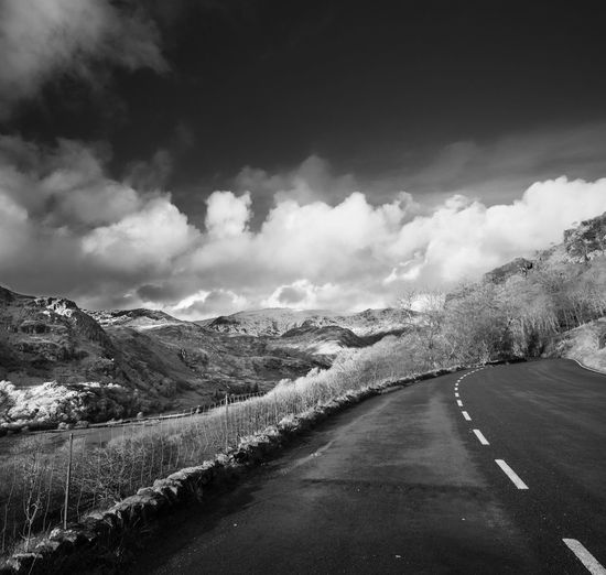 Road passing by mountains against cloudy sky