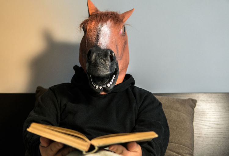 Man wearing horse mask while reading book