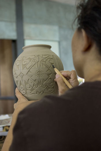 Rear view of woman carving on pot