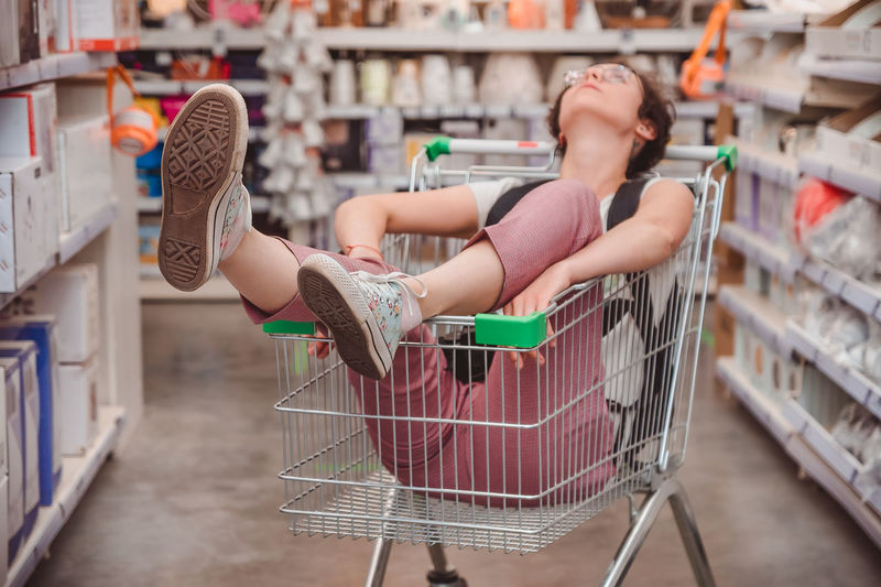 The girl is sitting in a basket in the shopping hall of the supermarket. riding in cart in store