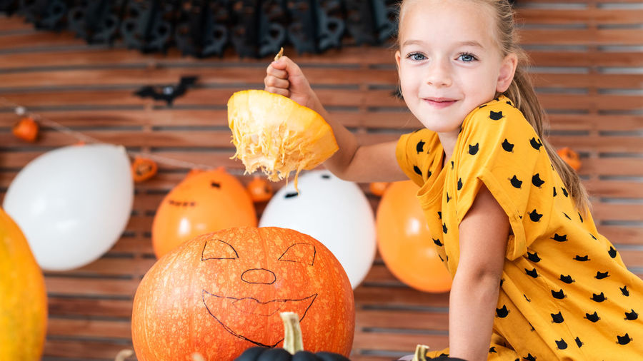 Portrait of cute girl sitting by pumpkin at home