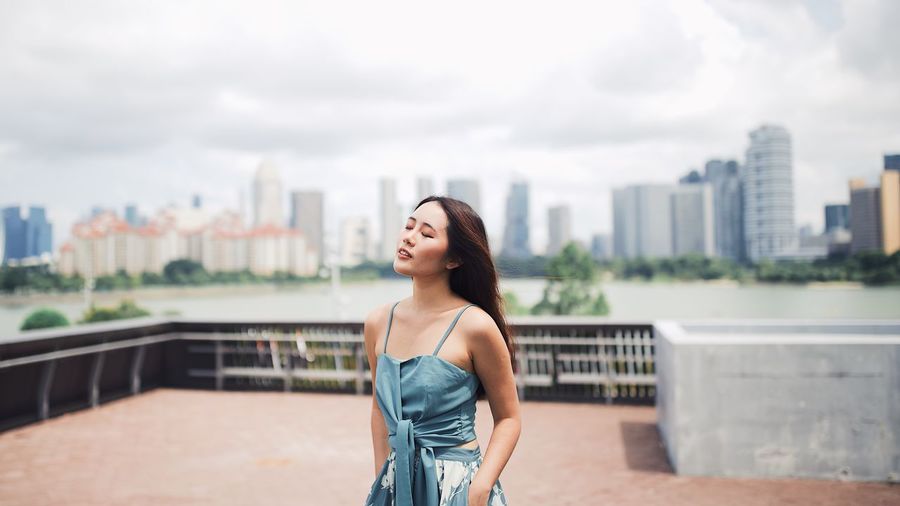 Young woman with eyes closed standing against cityscape and sky