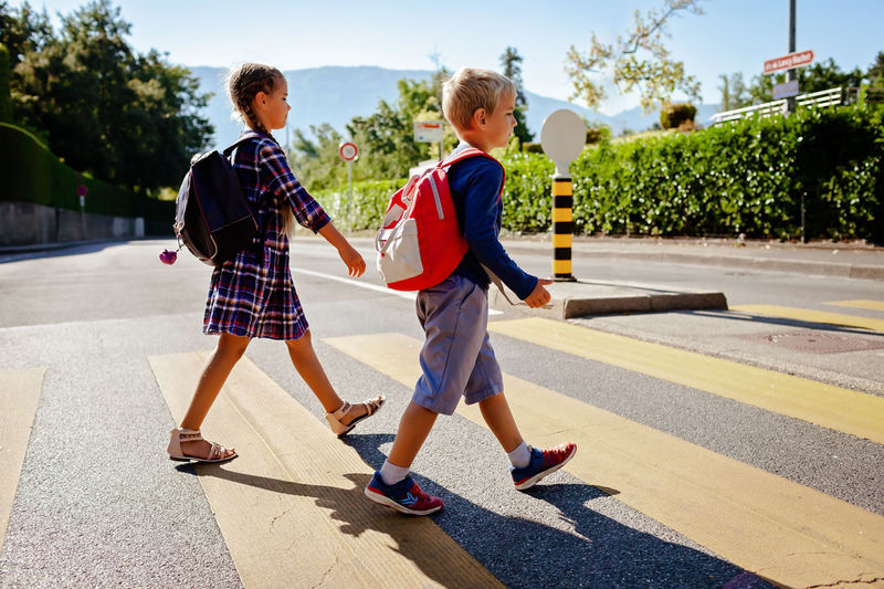 Kids with backpacks cross the road at crosswalk on the way to school. child safety, education