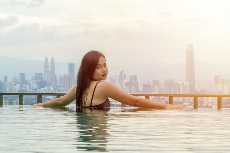 Young woman in swimming pool against buildings in city
