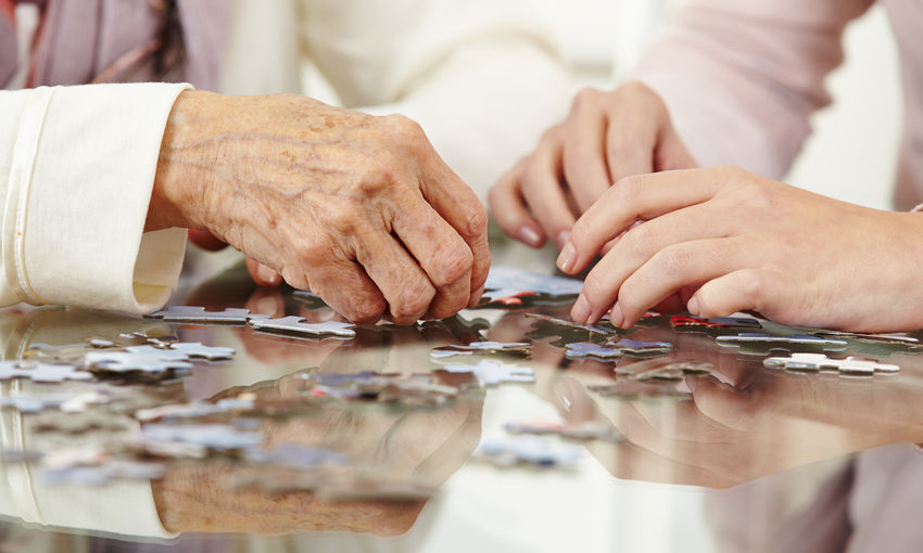 Midsection of grandmother and granddaughter solving puzzles on table at home