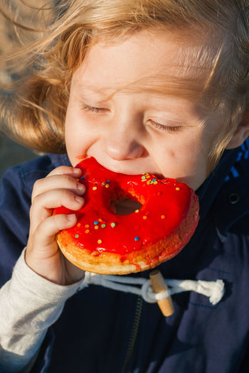 Girl in delight eats donut with red icing, food stained her mouth