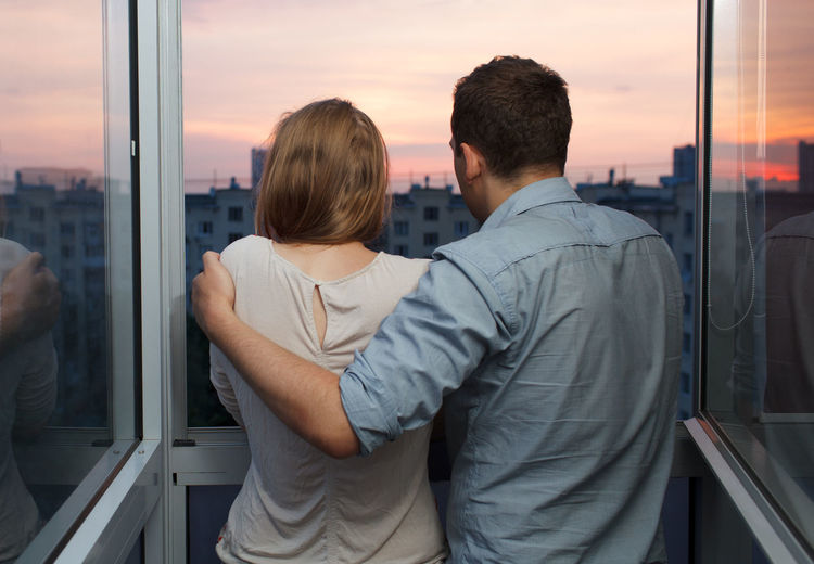 Rear view of man and woman looking through window during sunset