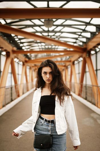 Portrait of beautiful young woman standing against bridge