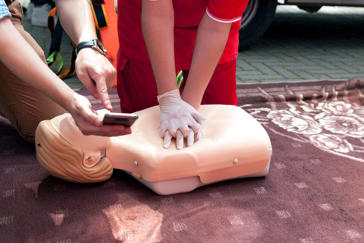 Midsection of man showing phone to woman practicing on cpr dummy