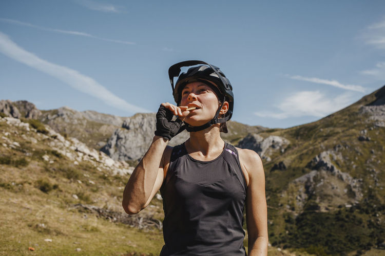 Woman wearing cycling helmet eating biscuit while standing against mountain at somiedo natural park, spain