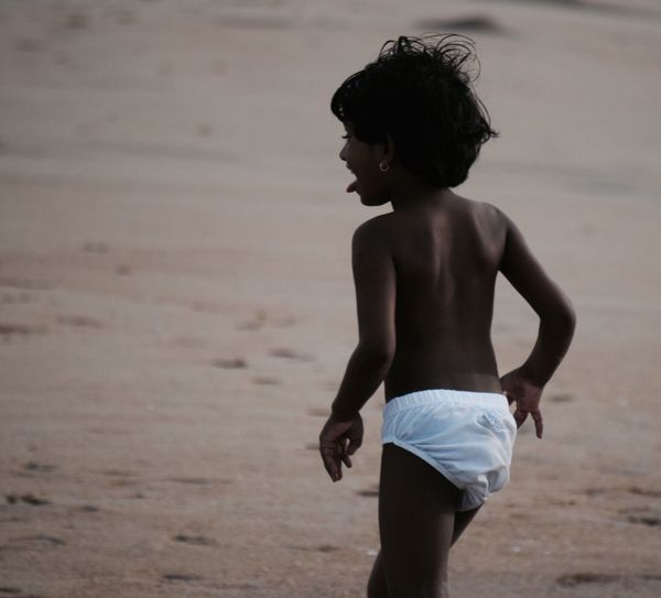 Rear view of playful shirtless girl walking at beach