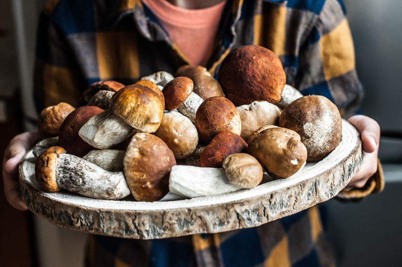 A large wooden dish with fresh forest mushrooms in children's hands.