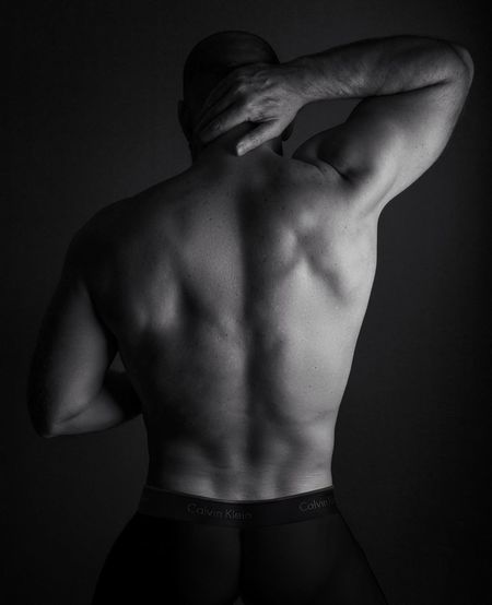 Rear view of shirtless man standing in darkroom