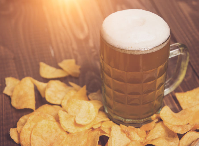 Close-up of beer glass with potato chips served on table