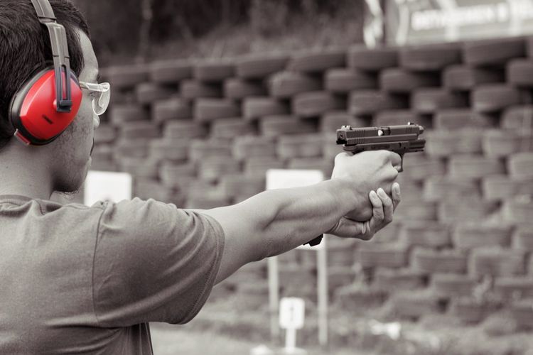 Side view of young man aiming handgun