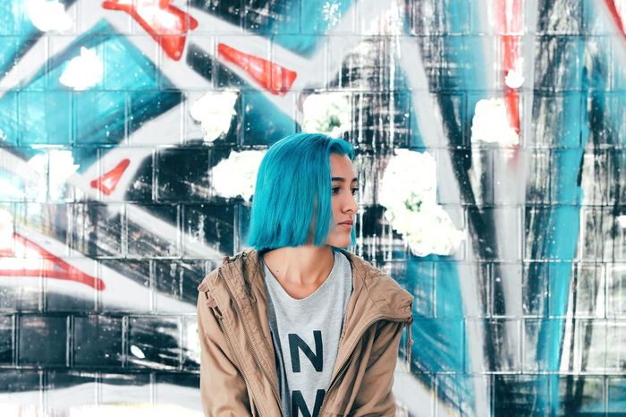 Woman with dyed hair sitting against graffiti wall