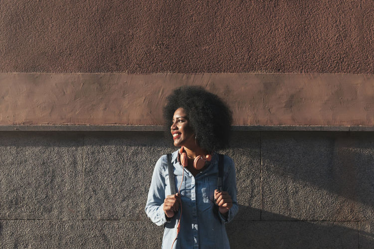 Smiling young woman standing against concrete wall