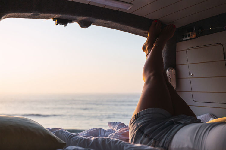 Woman relaxing while lying in camper van during sunset at beach