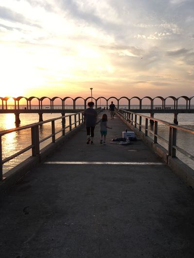 People walking on pier at sunset