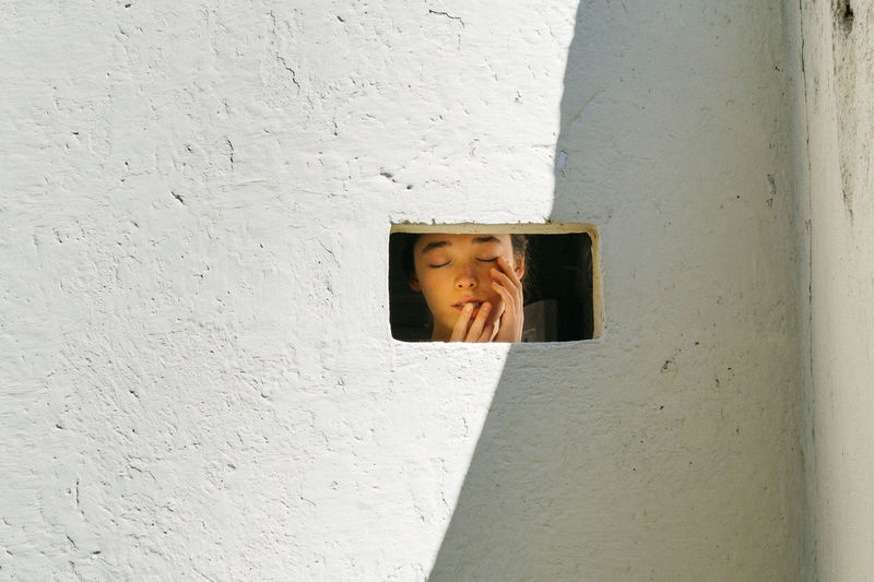 Girl with closed eyes seen through window
