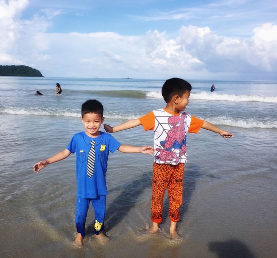 Happy siblings standing on beach against sky