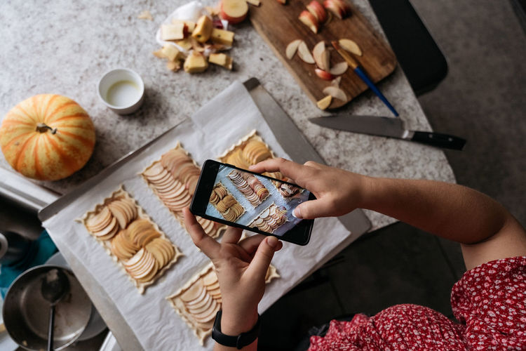 High view angle of female hands taking pictures of pastry with mobile phone
