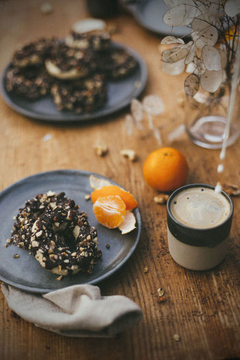 High angle view of fresh nut rings with chocolate on table with coffee and tangerine