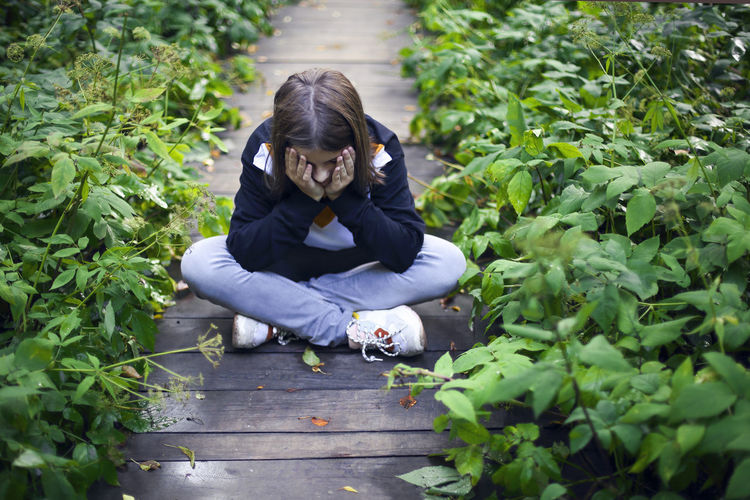 High angle view of teenage girl sitting on wooden pathway amidst plants
