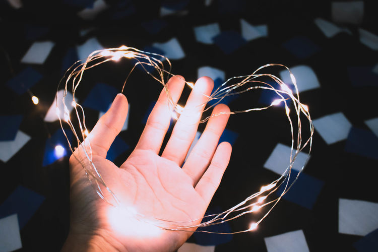 Cropped hand holding heart shape illuminated string light