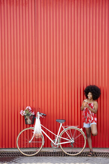 Side view of woman with bicycle standing against red wall