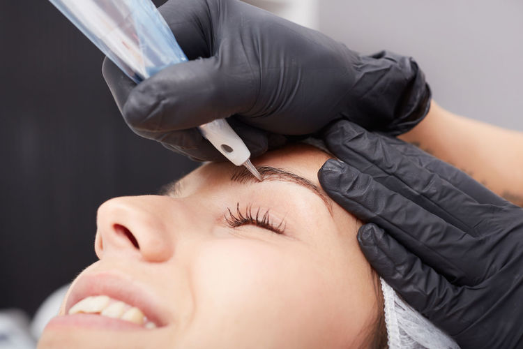 Cropped hands of beautician treating woman permanent eyebrow