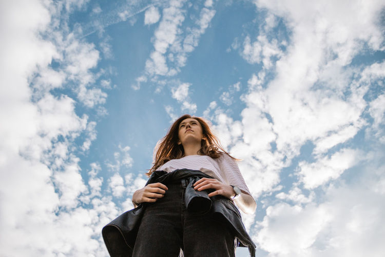 Low angle view of young woman standing against cloudy sky