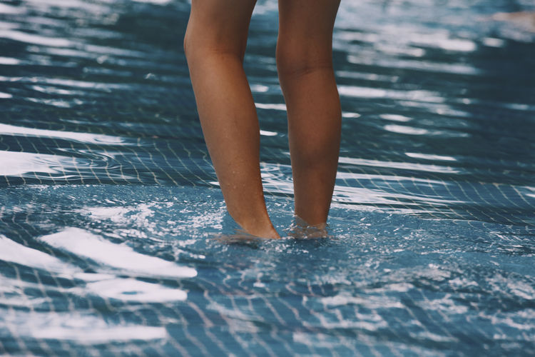 Close-up - a girl enters the blue water pool. 