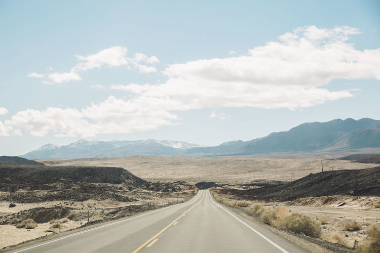 Empty road by mountains against sky