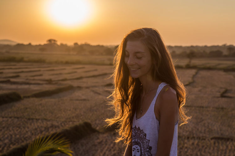 Portrait of beautiful young woman against sunset sky