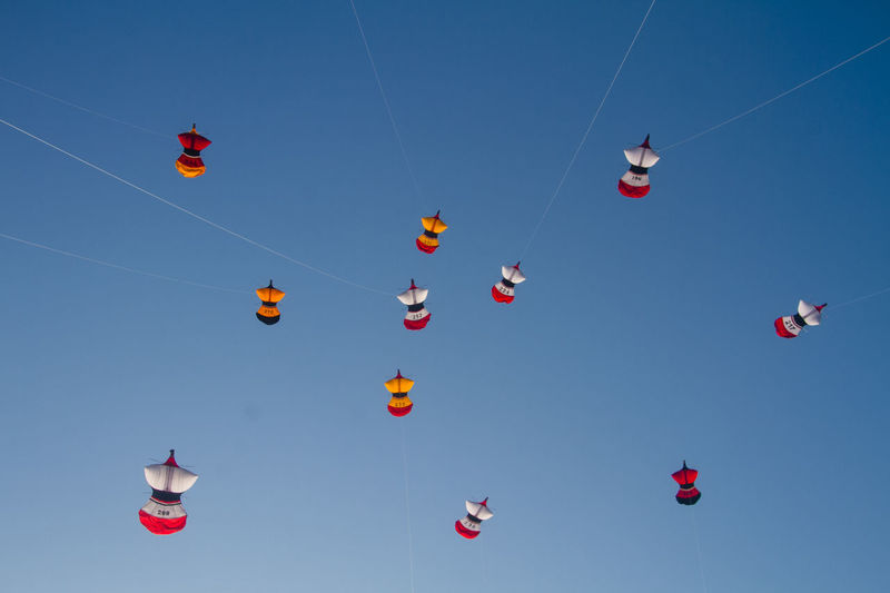 Low angle view of kites flying against clear blue sky