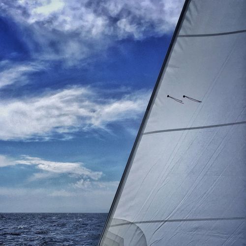 Tarpaulin sheet of sailboat on sea against wispy blue sky