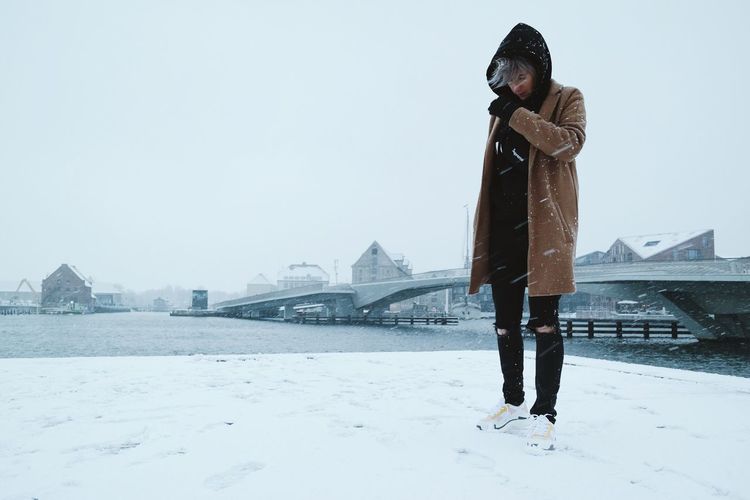Woman standing against bridge over river in city during snowfall