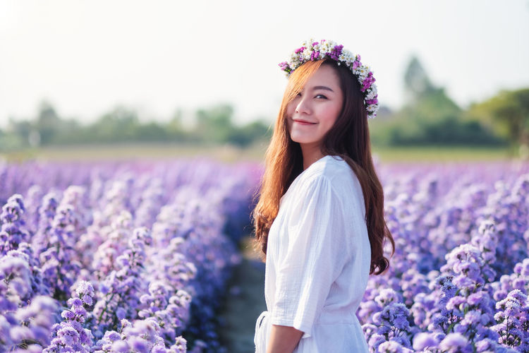 Portrait of woman standing by purple flower on field