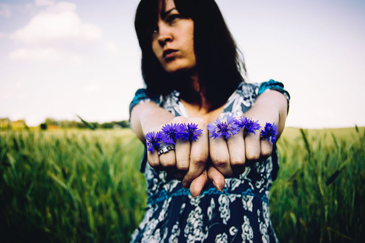 Young woman holding purple flowers in fist while standing on field