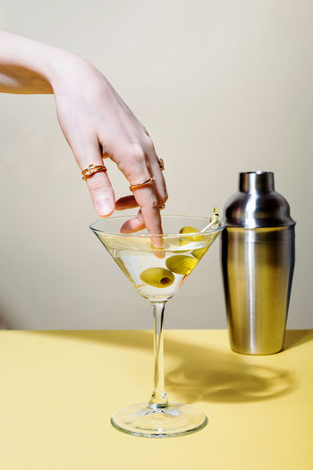 Woman dips finger with rings in glass of martini cocktail with olives