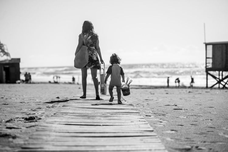 Rear view of people walking on boardwalk at beach against sky
