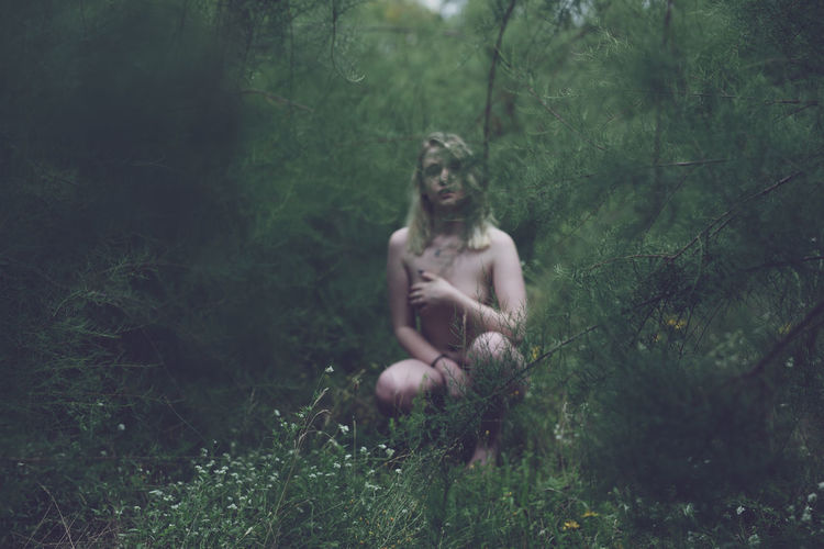 Young naked woman crouching in forest