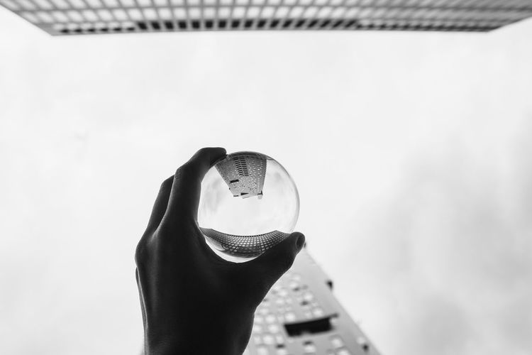 Cropped hand of person holding crystal ball with reflection of buildings