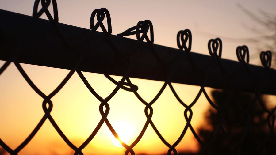 Close-up of chainlink fence against sky during sunset
