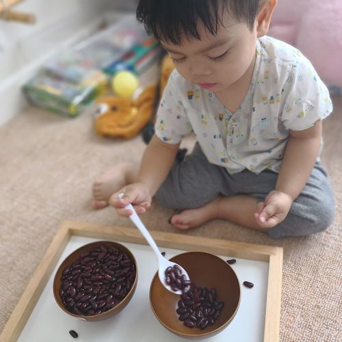 High angle view of boy putting kidney beans into bowl while sitting on floor at home